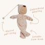 Olli Ella Lullaby Dozy Dinkum Doll - Luna is a baby doll with light brown skin, a tuft of brown hair, and a non-removable ballet pink soft velvet onesie with golden embroidered stars. Infographic.