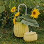 Close up of the Olli Ella eco-friendly rattan luggy trolley on some grass with some large sunflowers inside