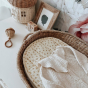 Close up of some knitted baby clothing laid out on top of an Olli Ella leafed mushroom luxe liner basket cushion, next to a rattan baby rattle
