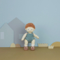 An Olli Ella Pea Dinkum Doll standing up with tehir arms out. They are pictured against a blue background with cutout house and grass shapes