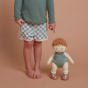 A close up of a child stood next to an Olli Ella Pea Dinkum Doll which is also standing up. The child is pointing at the doll