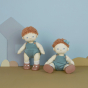 Two Olli Ella Pea Dinkum Dolls pictured against a blue background with cutout house and grass shapes. one doll is stood up, the other is sat down next to them wearing a blue coloured bow in their curly hair