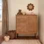 The Olli Ella Rattan Daisy Wall Basket in Natural Rattan on the wall, with a chest of draws in front and a selection of Olli Ella Tulip and Lily baskets on the floor. 