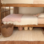 The Olli Ella Rattan Tulip Storage Basket in Natural, on a rug in a bedroom in front of a natural wood child's bunkbed.
