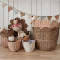 A full collection of Olli Ella baskets including the Olli Ella Rattan Tulip Storage Basket in Seashell Pink nesting inside the natural basket. Dozy Dinkum dolls are sleeping in the smaller baskets and there's bunting in the background.