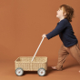 Young boy pushing the Olli Ella handmade rattan Wamble Walker on a brown background