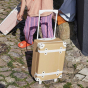 The Olli Ella See-Ya Suitcase in Butterscotch pictured on stone flooring outdoors a childs legs can be seen in the background 