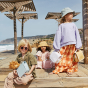 Children sitting on wooden decking near a beach holding the Olli Ella l See-Ya Wash Bags