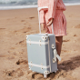 Child on a sandy beach holding the Olli Ella Steel Blue See-Ya Suitcase 