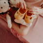 Close up of a childs hands holding the Olli Ella dinkum doll rubber shoes above a dinkum doll