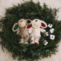 Cozy Dinkums Bunny Twiggy lying next to Cozy Dolls Twinkle, in a green wreath with white flowers