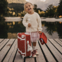 Child holding the Olli Ella See-Ya Washbag in Sweetheart Red design, with small white flowers on a red fabric background in one hand, and Olli Ella Travel Case in same design in other hand