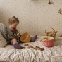 Young child sat on a bed playing with some wooden toys inside an Olli Ella woven rattan blossom basket