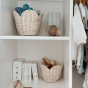The Olli Ella Rattan Lily Basket Set in Buttercream on the shelves of a wardrobe. One holds toys, the other is holding brushes.