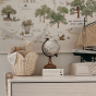 The Olli Ella Rattan Lily Basket Set in Buttercream on a chest of draws in a nursery, nesting together holding baby essentials. There's a globe and wooden toy ship next to them and map on the wall.