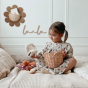 A child is sat on the bed with the Olli Ella Rattan Lily Basket Set in Seashell Pink taking out soft toys. 