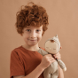 Close up of a boy smiling and holding an Olli Ella plush Dozy Dinkum toy in front of a brown background