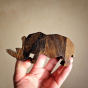 Close up of hand holding O-WOW eco-friendly dark oak Rhino toy in front of a beige background