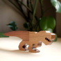 Close up of O-WOW sustainable Walnut T-Rex dinosaur toy on a white floor in front of some green plants