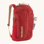 Patagonia Recycled Black Hole Backpack 25L in Touring Red with a map in the front zipper pocket and small essentials in the lid pocket on a cream background 