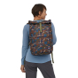Woman stood backwards on a white background wearing the Patagonia sisu brown, mushroom forest print roll top arbor pack