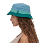 Woman stood sideways on a white background wearing the Patagonia organic cotton light blue bucket hat