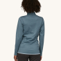 A woman models the back of the Patagonia Women's R1 Daily Jacket - Light Plume Grey / Steam Blue X-Dye against a plain background.