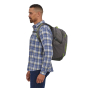 A man wearing the Patagonia Refugio Day Pack 26L in Forge Grey, stood upright, side view on white background