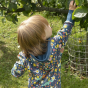 Child reaching up to touch some leaves wearing the Piccalilly hooded galaxy print playsuit