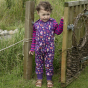 Young girl stood next to a wooden gate wearing the Piccalilly organic cotton woodland print dungarees