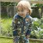 Child stood in front of some green plants wearing the Piccalilly galaxy print hooded playsuit 