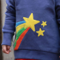 close up of a child wearing blue organic cotton sweatshirt with a fabulous shooting star with a rainbow tail applique design on the front from piccalilly