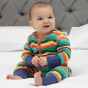 baby wearing organic cotton footless onesie with a bright rainbow stripe print and stretchy blue cuffs from piccalilly