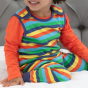 close up of toddler wearing organic cotton dungarees for babies and toddlers with a bright rainbow stripe all-over print, a co-ordinating blue trim and comfy stretchy cuffs from piccalilly