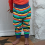 child wearing organic cotton baby and toddler bottoms with a bright rainbow stripe design with a co-ordinating blue waistband and stretchy cuffs that fold up from piccalilly