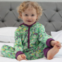 child wearing green organic cotton hooded playsuit with the spring meadow print and purple lining from piccalilly