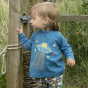 Young child stood holding on to a wooden fence post wearing the Piccalilly blue long sleeve alien top