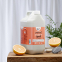 Bio-D Pink Grapefruit scented natural Washing Up Liquid in a 5 litre refill bottle on a wooden table with cut grapefruit, and a white background