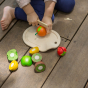 Close up of child outside on decking cutting up pretend play food from the PlanToys Assorted Fruit Set.