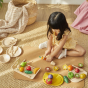 Child sat on a mat  cutting up pretend play food from the PlanToys Assorted Fruit Set and other PlanToys wooden play food sets.
