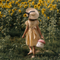 Picture of a child holding the Olli Ella Mushroom Rattan basket in a field of sunflowers.