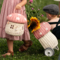 Picture of a childholding the Olli Ella Mushroom Luggy and the Mushroom Basket, with sunflowers.