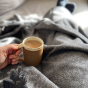Close up of a hand holding a mug of coffee on top of the Respiin recycled wool grey throw blanket