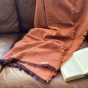 Orange Respiin woollen throw draped over a leather sofa next to an open book