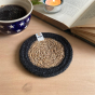 Close up of a Respiin handmade jute coaster in the black and natural colour next to an open book