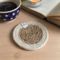 Close up of a Respiin handmade jute and seagrass coaster on a wooden table next to an open book