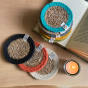 Coloured Respiin handmade jute coasters stacked on an open book next to a small orange candle