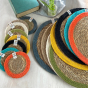 Colourful stack of handmade Respiin jute and seagrass coasters and placemats on a white wooden table next to a book and potted plant