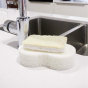 Seep natural cellulose loofah scourer on top of a white kitchen sponge next to a kitchen sink