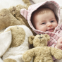 A child happily laying next to the Senger Animal Baby Bear Toy, and the Cuddly Rabbit and Camel toy